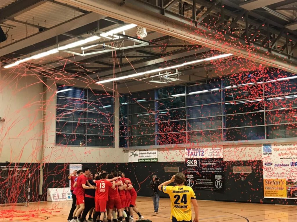 In der Riesener-Halle: Confettinebel in rot, Handballer liegen sich in den Armen