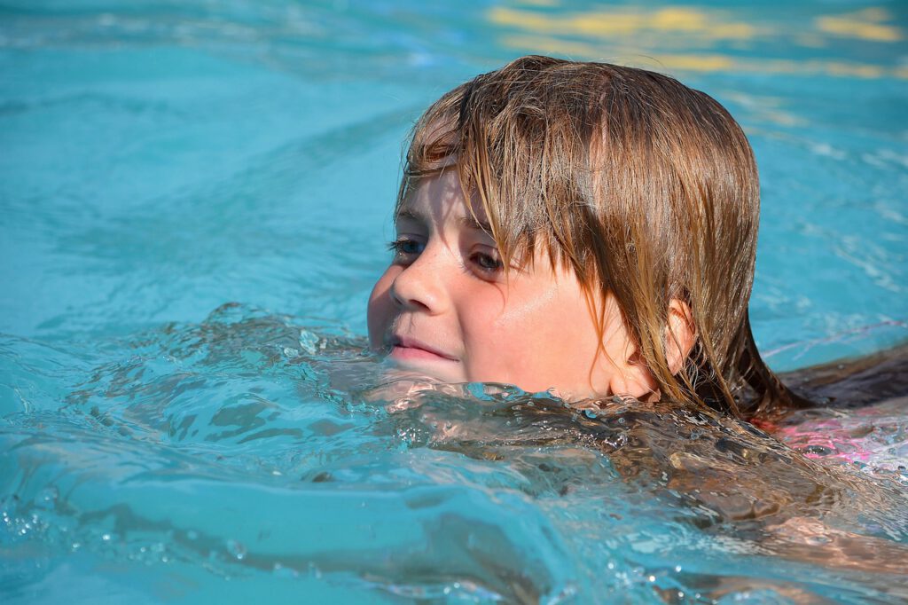 Großaufnahme eines kleinen, lächelnden Mädchens mit nassen Haaren beim Brustschwimmen